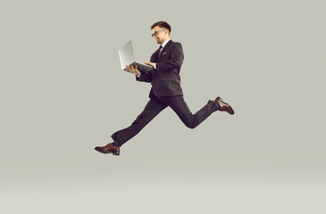 Fototapeta na wymiar Competition in business. Successful young businessman who is in hurry to do lot of work working on laptop on run. Man in suit and glasses looking to enhance his career is isolated on gray background.