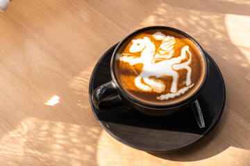 Hot coffee latte with latte art in the form of a horse milk foam in cup mug on wood desk on top view. As breakfast In a coffee shop at the cafe,during business work concept