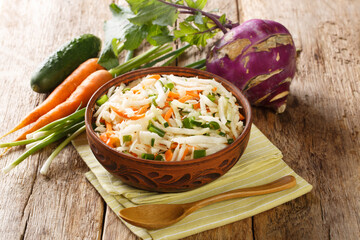 Raw salad of kohlrabi, carrots, cucumbers and green onions seasoned with oil close-up in a plate on a wooden table. Horizontal