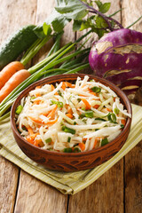 Fresh salad of kohlrabi, carrots, cucumbers and green onions close-up in a plate on a wooden table. Vertical