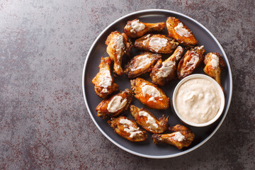 Portion of grilled chicken wings with Alabama white barbecue sauce close-up in a plate on the...