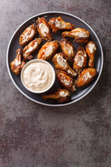Grilled chicken wings with Alabama white sauce close-up in a plate on the table. Vertical top view from above