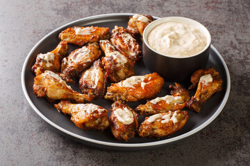 Portion of grilled chicken wings with Alabama white barbecue sauce close-up in a plate on the table. Horizontal