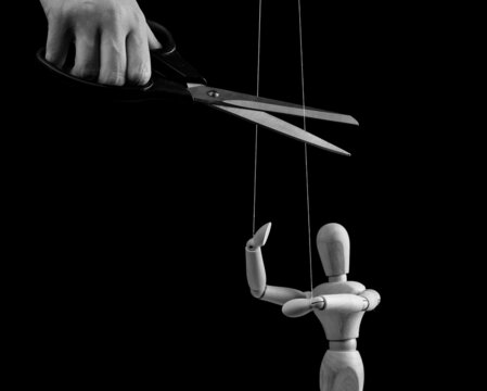 Hand Cutting Strings Over Puppet With Scissors. Manipulation, Negative Influence, Control Stop Concept. Overcoming Addiction. Black And White. High Quality Photo