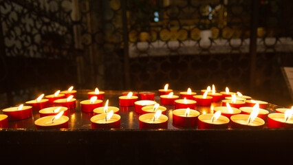 Perspective of a multitude of burning candles with flames in a italian cathedral, posed by believers after a prayer.