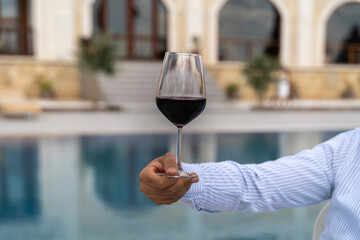 A glass of wine at a man's hand in front of a swimming pool