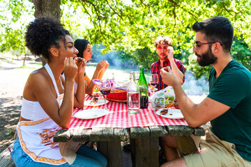 Young multiethnic friends eating chicken skewers at park - Barbecue Grilled meat skewers with...
