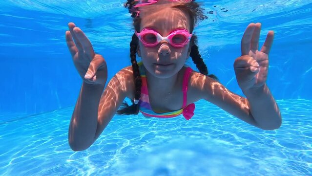 Little girl study to swim underwater in pool. show by fingers ok. Child in colored bikini and pink glasses. Sport good for healthy. having fun in the pool. show by hands fingers ok. vacation concept