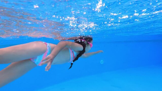 Little girl deftly swim underwater in pool. Child in blue with pink swimsuit spins and holds breath. Sport good for healthy. Concept vacation and hobby.
