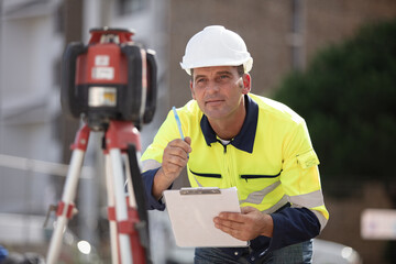 surveyor with clipboard crouched by a theodolite