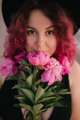 Young woman with pink hair holding bunch of peonies on the beach.