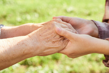 hands of a young woman hold the hands of a grandmother close-up.