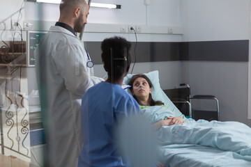 Sick woman patient discussing with medical doctors while resting in bed during illness recovering...