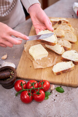 Woman spreading tasty organic butter onto bread over grey table with wooden cutting board