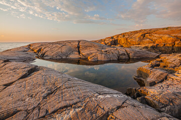 Sunset over smooth-cut bare granite rocks with small pond at the coast of the Barents sea in the vicinity of Grense Jakobselv, Finnmark, Norway
