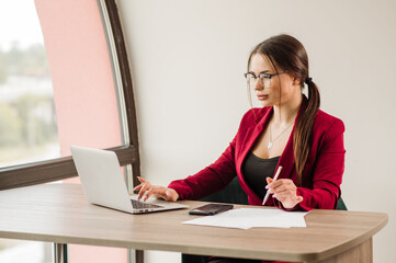 Female office worker or secretary is working with a laptop on the office desk. Portrait of sexy office worker