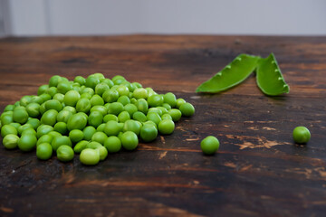 Fresh peeled green pease on a brown wooden table with copy space. Still life of green peas in pods with pea shoots on wooden table