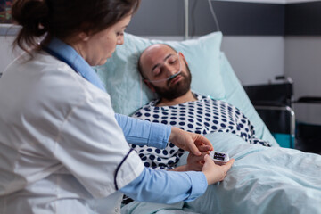 Close up of sick man patient lying in bed with medical oximeter on finger. Woman doctor monitoring...