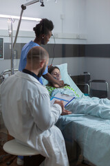 Fototapeta premium Practitioners team checking patient putting oxigen mask monitoring respiratory illness during coronavirus pandemic in hospital ward. Nurse with black skin checking heart puls using medical stethoscope