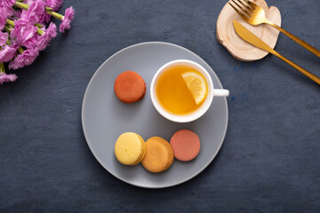 Smile with macaroons and cup tea on a plate on a dark stone table with flowers. Beautiful delicious dessert