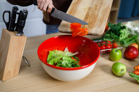 Girl preparing a salad of fresh lettuce and vegetables throwing chopped red peppers into a bowl