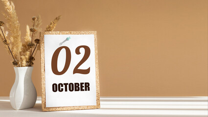october 2. 2th day of month, calendar date.White vase with dead wood next to cork board with numbers. White-beige background with striped shadow. Concept of day of year, time planner, autumn month