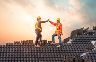 A team of male roofers use a cordless electric battery drill to fire screws to install concrete roofing slabs or c-packs on home structure construction they happy after work success - obrazy, fototapety, plakaty