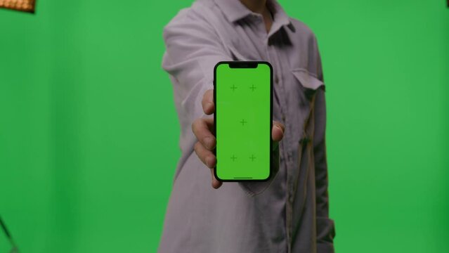 Man showing a smartphone with green screen while standing over an isolated background.