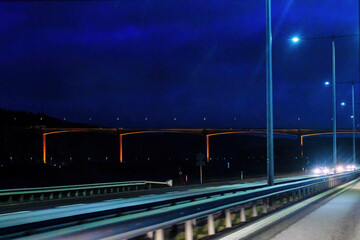 motorway at night approaching a huge bridge, lit orange against dark blue skies