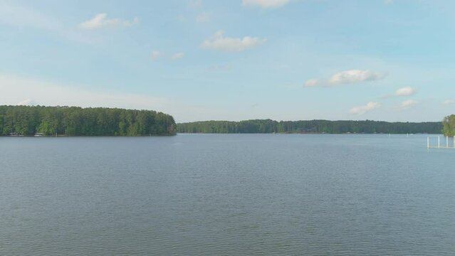 aerial footage of the vast blue rippling waters of Lake Acworth surrounded by lush green trees, grass and plants with blue sky and clouds at Proctor Landing Park at Lake Acworth in Acworth Georgia USA
