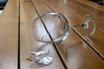 Broken crystal wine glass on a wooden table. Crystal shards next to a broken glass