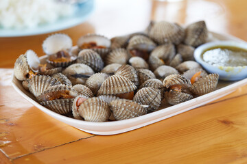 Boiled cockles and spicy and sour seafood sauce served on a white plate and placed on a wooden table, seafood popular in Thailand, local food.