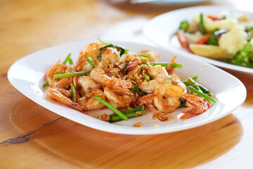 Fried shrimp with garlic and vegetables in white plate on wooden table, seafood.