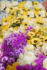 Patterns of artificial flowers of various colors (purple, yellow, white, cream) are arranged together to decorate. (Sunflowers, cream roses, and purple orchids)