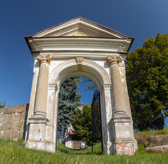 Fototapeta na wymiar Classicist gate at the entrance to a country cemetery with a baroque chapel