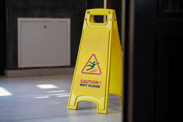 Yellow sign showing warning of caution wet floor. Slippery sign on wet floor in office building