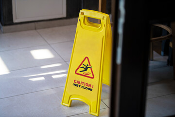 Yellow sign showing warning of caution wet floor. Slippery sign on wet floor in office building