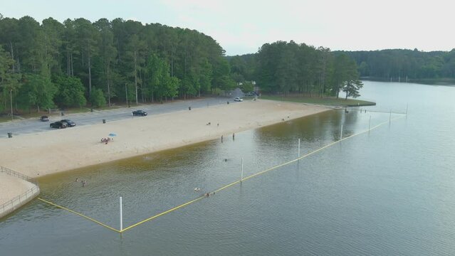 aerial footage of the silky brown sand of the beach surrounded by rippling lake water and lush green trees, grass and plants at Proctor Landing Park at Lake Acworth in Acworth Georgia USA