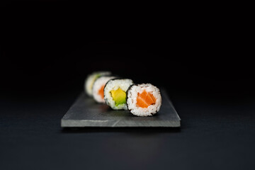 Sushi composition with salmon, avocado and cucumber. Sushi roll on a black background.