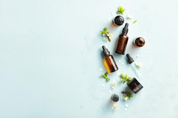 Amber glass cosmetic bottles mockups with water drops and spring flowers on blue background. Natural organic beauty product packaging design.