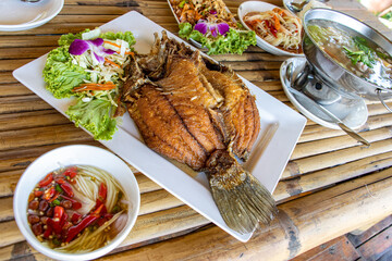 Traditional Thai food, grilled fish, soup, vegetables and rice on bamboo table.
