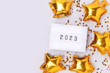 Lightbox with 2023 numbers on a blue background with copy space. Golden confetti and stars foil balloons.