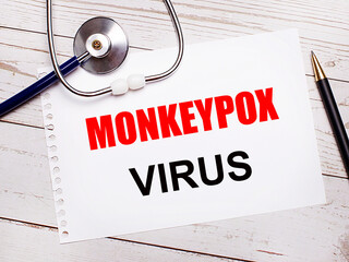 On a light wooden table there is a stethoscope, a pen and a sheet of paper with the text MONKEYPOX VIRUS. Medical concept