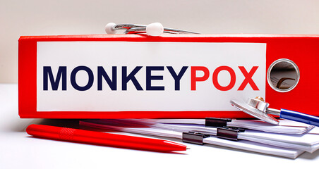 On the desktop is a stethoscope, documents, a pen, and a red file folder with the text MONKEYPOX. Medical concept