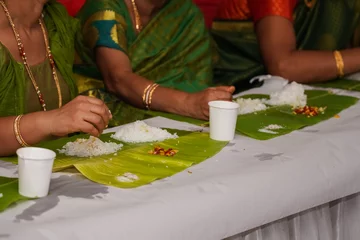 Foto op Canvas Traditional South Indian food served on banana leaves, selective focus on the staple food - rice. Traditional Indian outfits and jewelry worn by the women out of focus © Sahana
