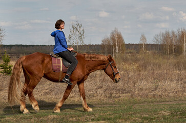 Woman in casual clothes rides a horse in early spring