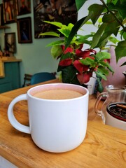 White cup of coffee with foam in a cafe in front of flowers