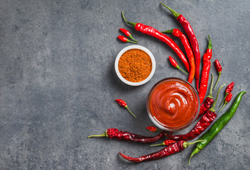 Chili sauce ketchup in bowl and fresh chili peppers and dry flakes spices on dark background copy...