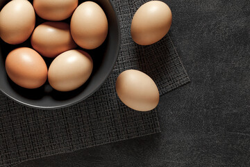 Eggs chicken, beige, whole, in bowl, grey tablecloth, on dark background, top view, space to copy text.