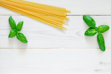 Spaghetti, raw pasta, basil leaves on white wooden board background, top view, space to copy text.